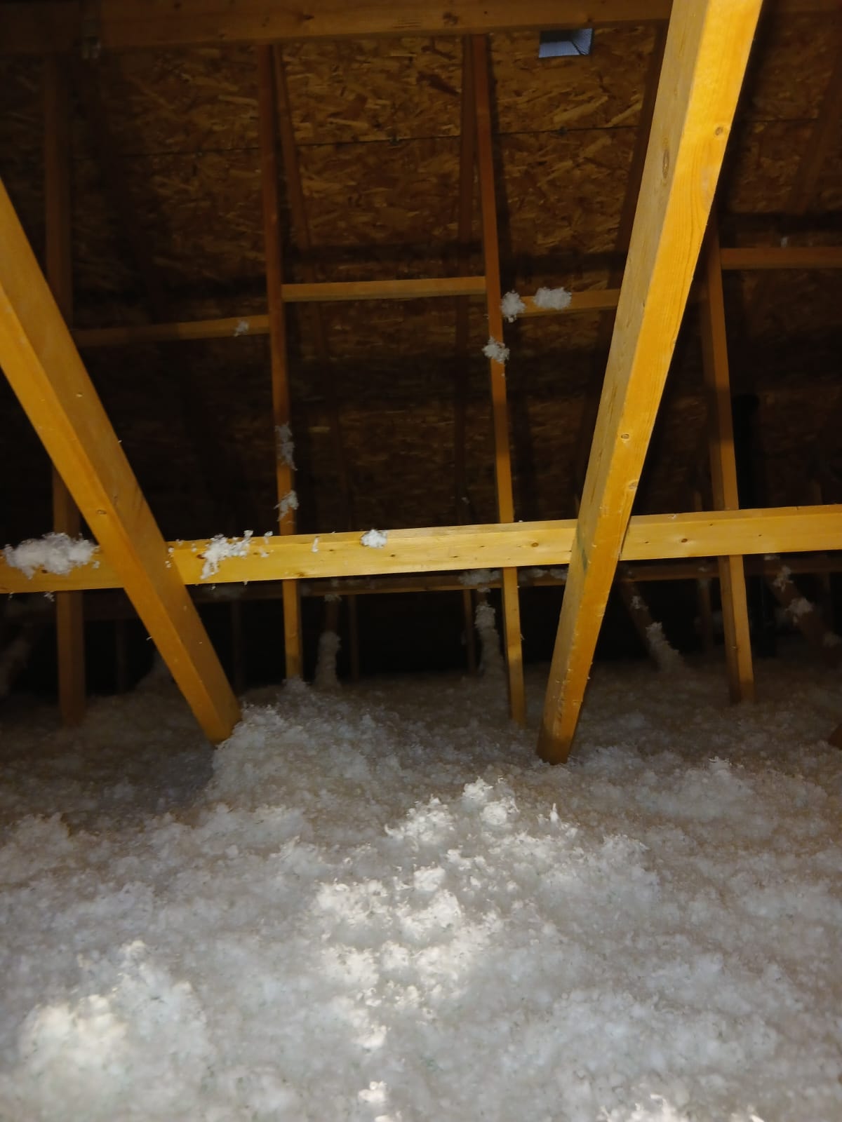 Blown-in attic insulation between yellow support beams